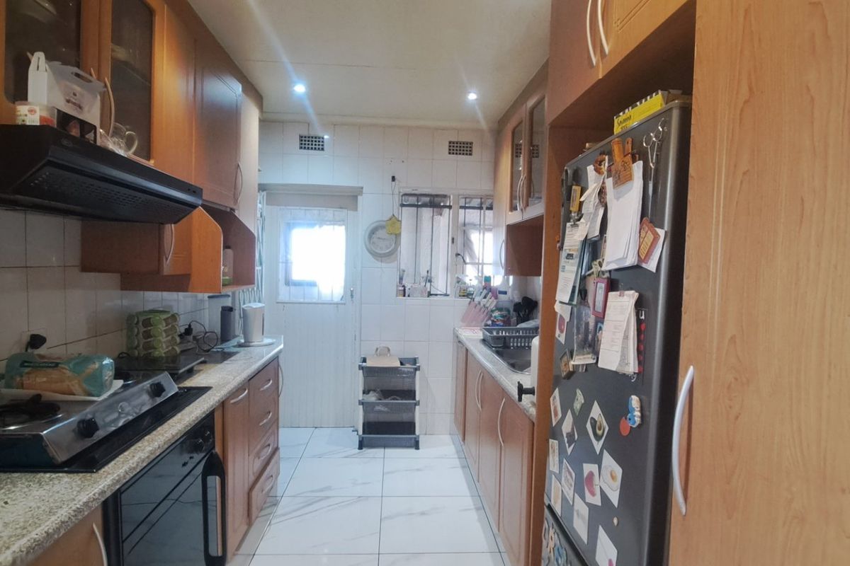 A functional galley-style kitchen featuring wood-finish cabinetry, a gas hob with extractor fan, tiled flooring, and a tiled backsplash.