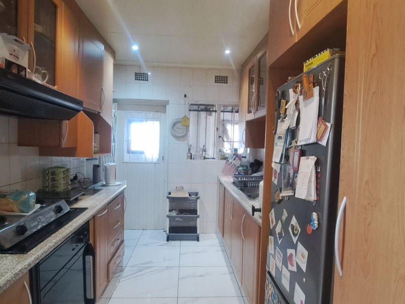 A functional galley-style kitchen featuring wood-finish cabinetry, a gas hob with extractor fan, tiled flooring, and a tiled backsplash.