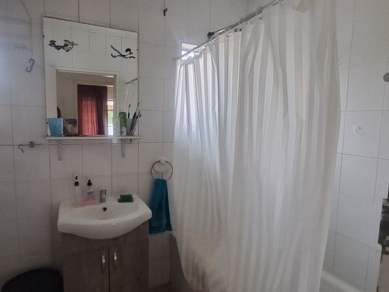 A functional bathroom featuring a vanity basin, tiled walls, and a shower-over-bath configuration, currently showing signs of wear and wall surface damage.