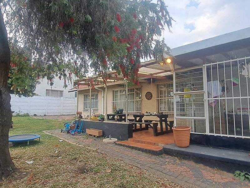 Rear view of the property featuring a covered patio area, paved walkway, and a spacious garden with established trees and security features.
