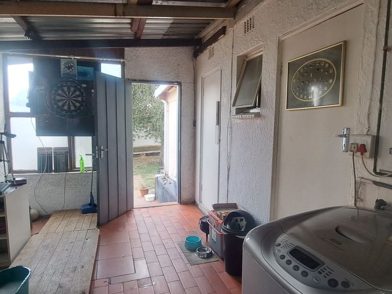 A functional laundry area featuring tiled flooring, exposed ceiling beams, and direct access to the rear garden.