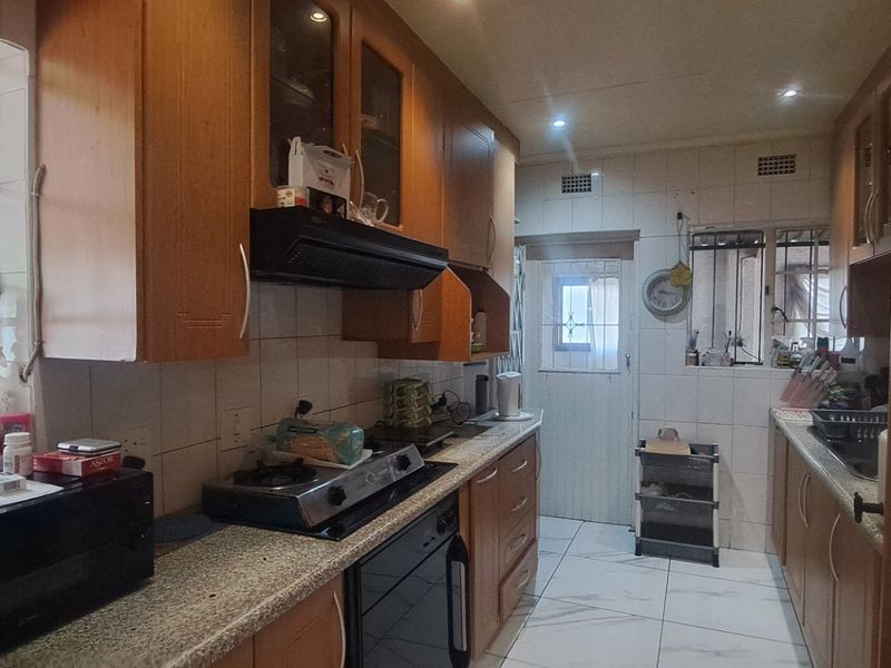 A functional kitchen featuring wooden cabinetry, granite countertops, a gas hob with extractor fan, and tiled flooring with access to an exterior door.