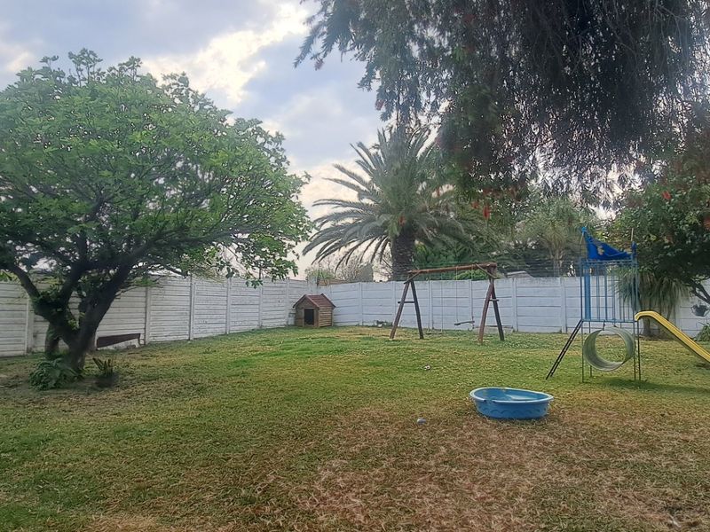 A spacious rear garden featuring a large lawn, mature trees, and a secure precast concrete boundary wall.