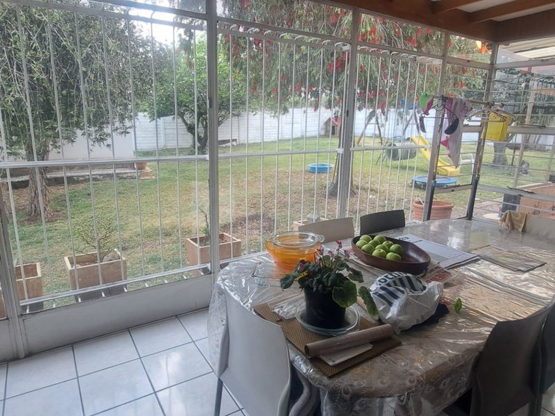 An enclosed patio area featuring tiled flooring, metal security bars, and a translucent roof, offering a view of the rear garden.