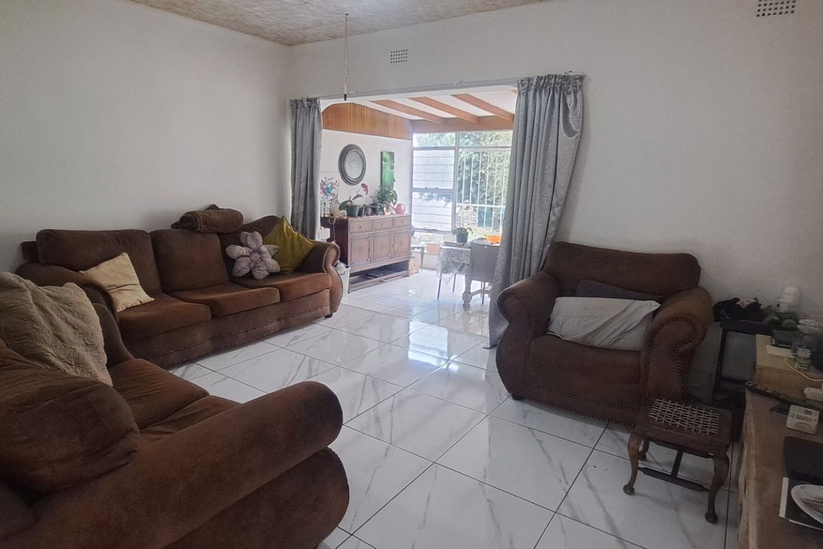 A spacious living room featuring white tiled flooring and a sliding door leading to an adjacent sunroom or patio area.