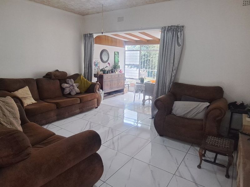 A spacious living room featuring white tiled flooring and a sliding door leading to an adjacent sunroom or patio area.