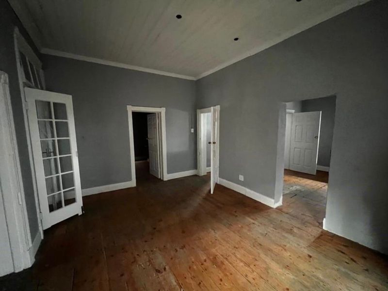 An empty living area featuring original timber flooring, classic french doors, and multiple access points to adjacent rooms.