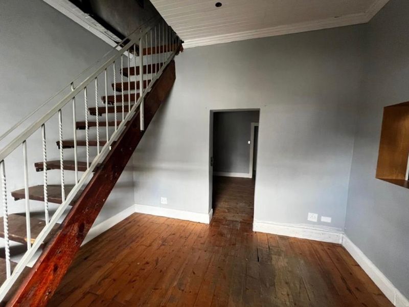 An empty living area featuring original timber flooring, a wooden staircase with metal balustrade, and access to an adjoining room.