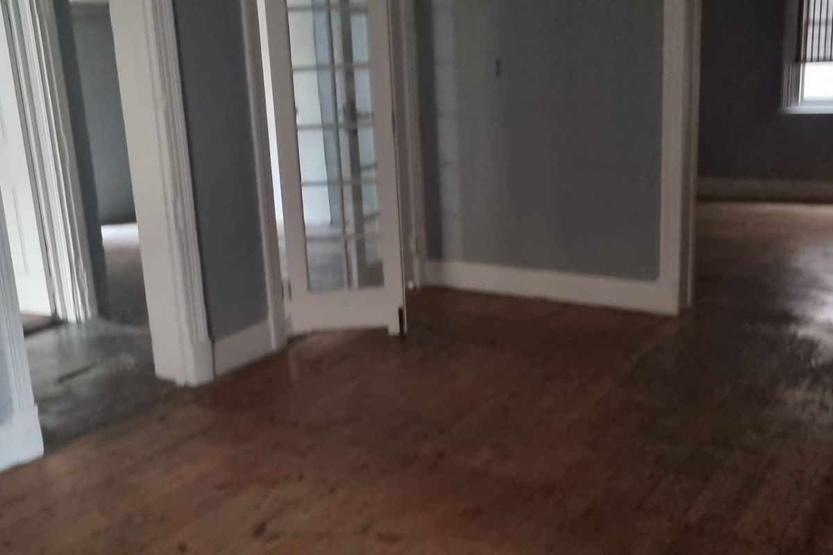 An empty living area featuring original hardwood flooring, classic architraves, and glass-paneled french doors leading to adjacent rooms.