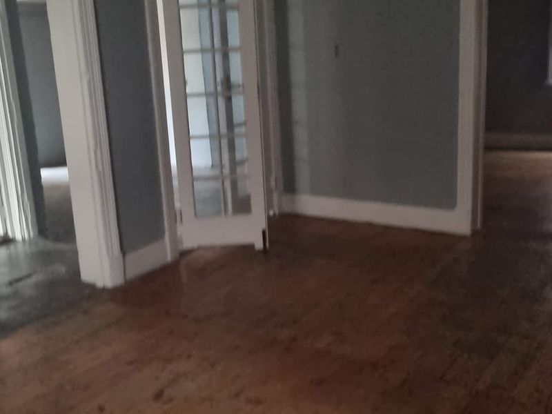 An empty living area featuring original hardwood flooring, classic architraves, and glass-paneled french doors leading to adjacent rooms.