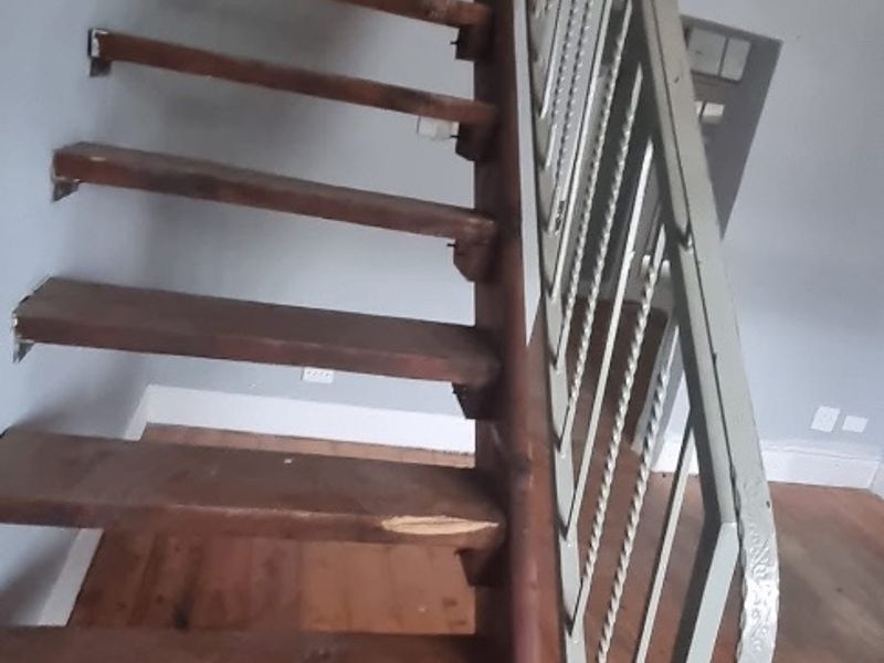 A steep timber staircase with a wrought iron balustrade leading to an upper level, featuring original timber flooring and visible wear.