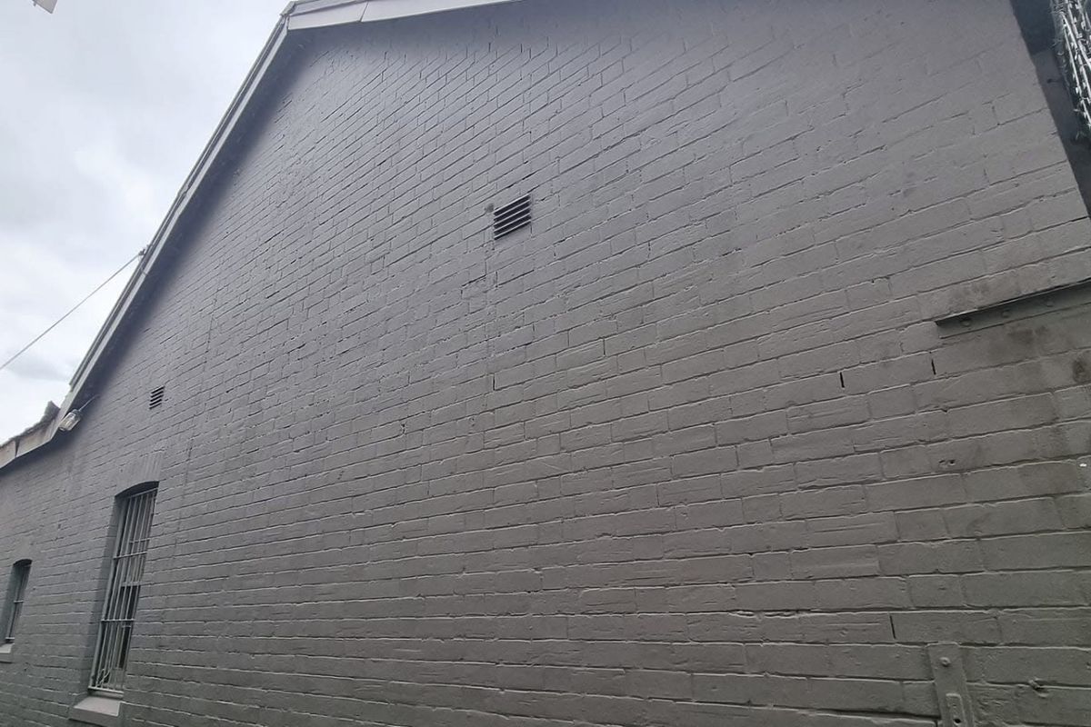 Side view of a commercial building featuring painted brick walls, security bars on windows, and integrated ventilation grilles.