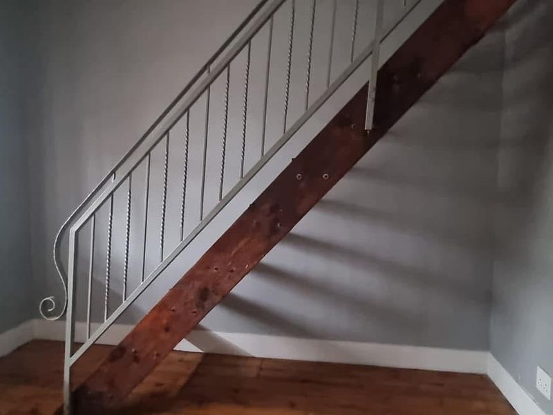 An interior hallway space featuring a timber staircase with a decorative metal balustrade and polished timber flooring.