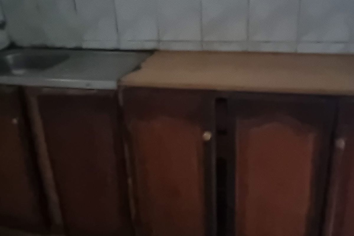 A small kitchen area featuring built-in wooden cabinetry, a stainless steel sink, and a tiled backsplash, currently in need of cosmetic updates.