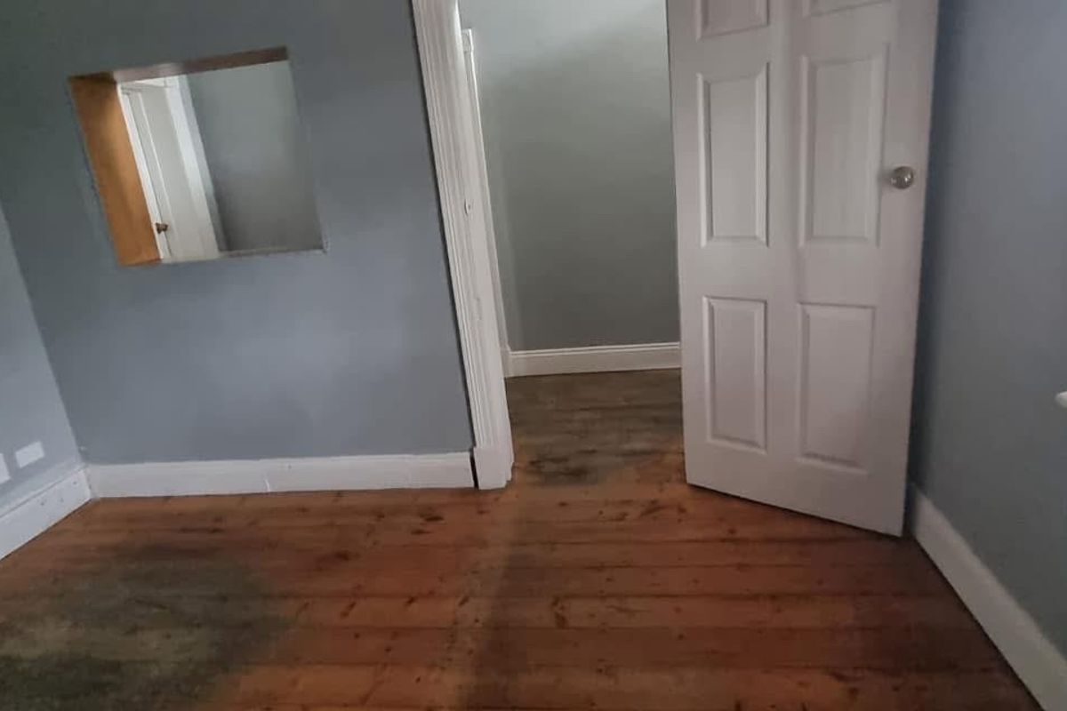 An empty bedroom featuring original timber flooring, a wall cutout, and a standard internal door, requiring cosmetic updates to the flooring and paintwork.