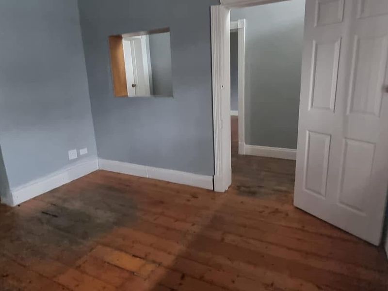 An empty living room featuring original timber flooring, neutral wall paint, and a unique wall cutout connecting to adjacent spaces.