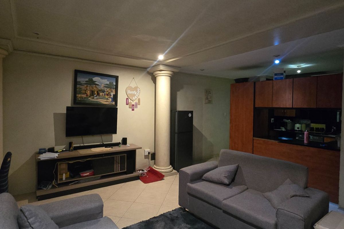 Open-plan living area featuring tiled floors, decorative columns, and an integrated kitchen with wooden cabinetry.