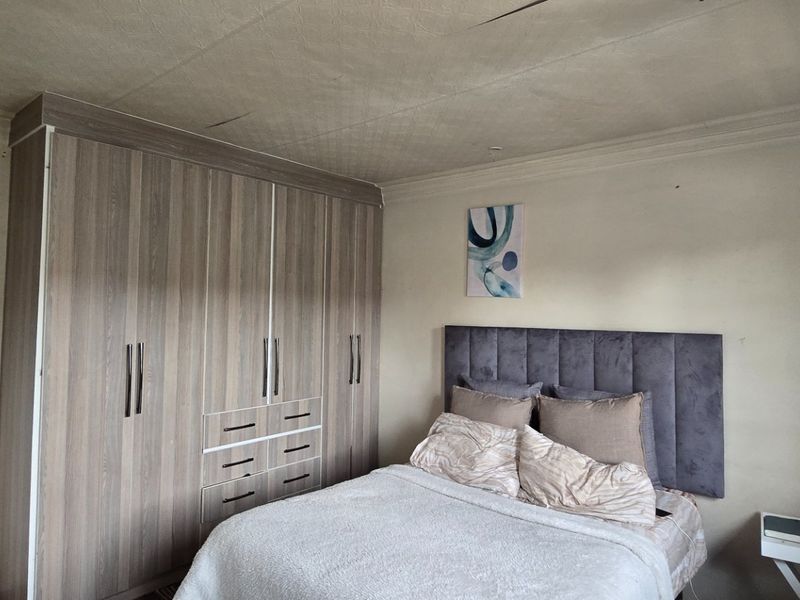 A bedroom featuring built-in wooden cupboards and a textured ceiling with visible cracks, requiring maintenance and cosmetic updates.