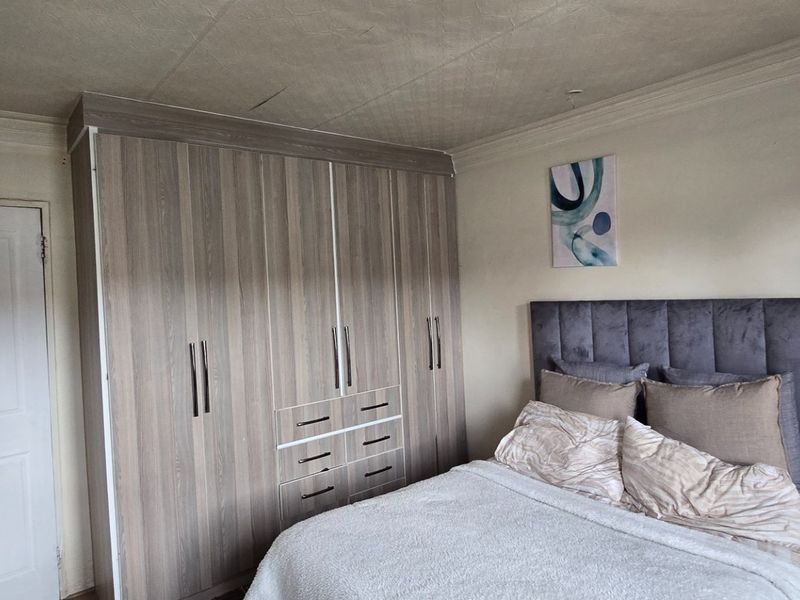 A bedroom featuring built-in wooden cupboards and crown molding, showing signs of wear on the ceiling.