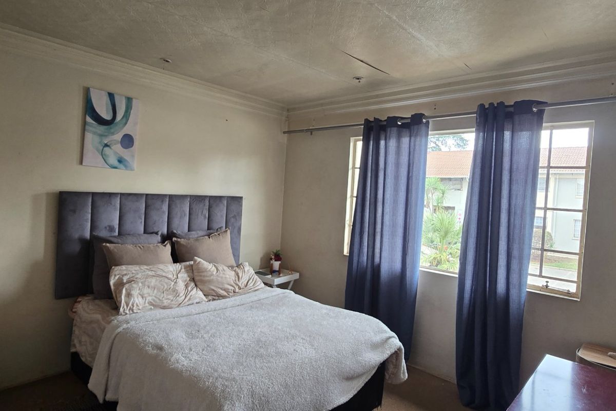 A bedroom featuring a built-in wardrobe and window, showing signs of wear including ceiling cracks and paint deterioration.