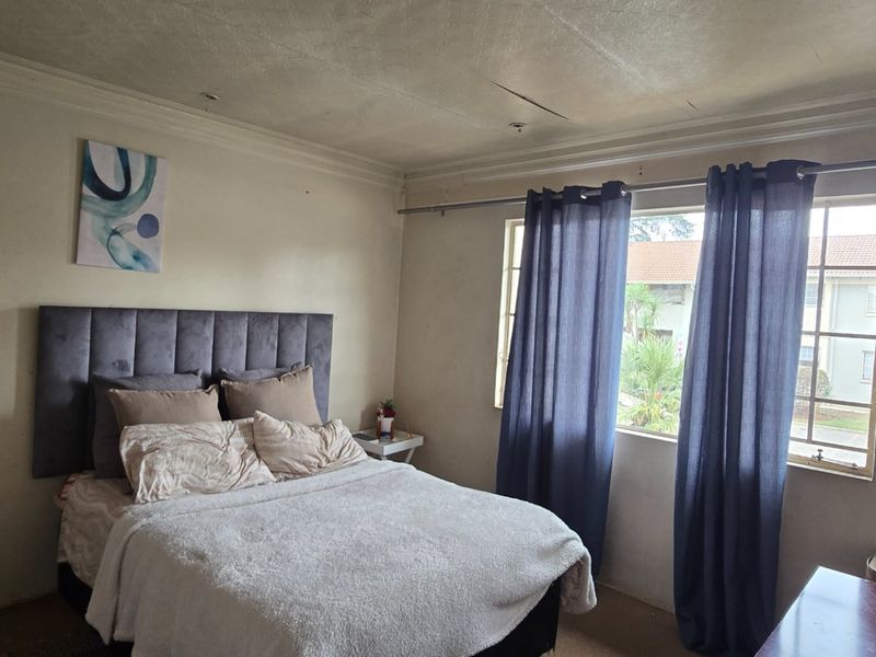 A bedroom featuring a built-in wardrobe and window, showing signs of wear including ceiling cracks and paint deterioration.