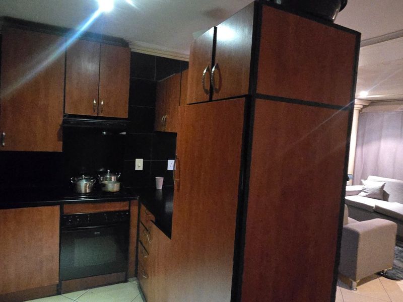 Open plan kitchen and living area featuring dark wood cabinetry, built-in oven, and tiled flooring in a functional apartment layout.