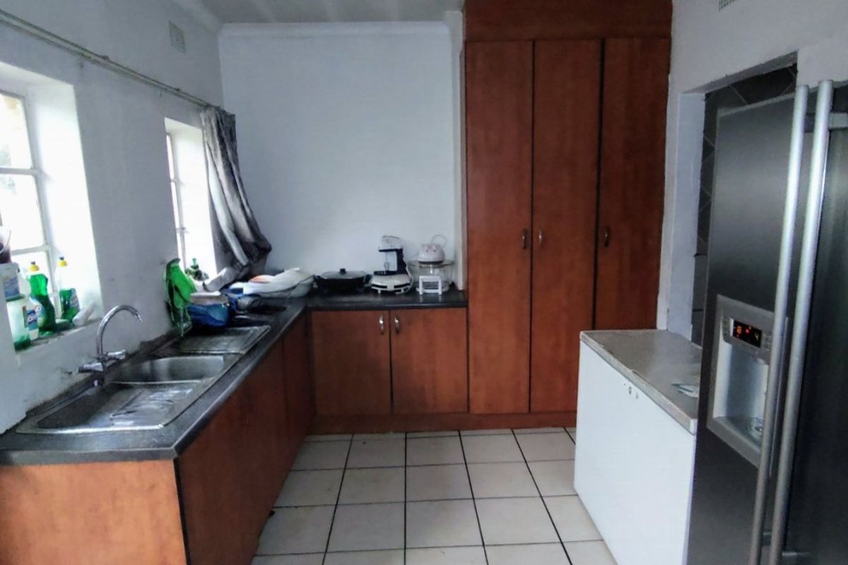 A functional kitchen featuring wooden cabinetry, a double sink, and tiled flooring, offering a practical layout with potential for modern updates.