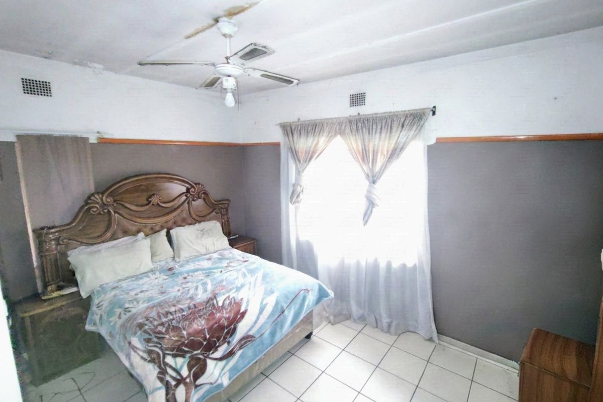 A bedroom featuring tiled flooring and a ceiling fan, showing signs of ceiling water damage and wear requiring maintenance.