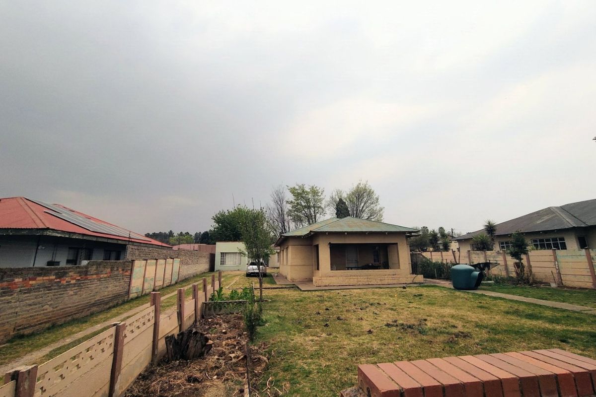 Rear view of the property featuring a detached dwelling with a covered patio, set within a large garden enclosed by precast concrete boundary walls.