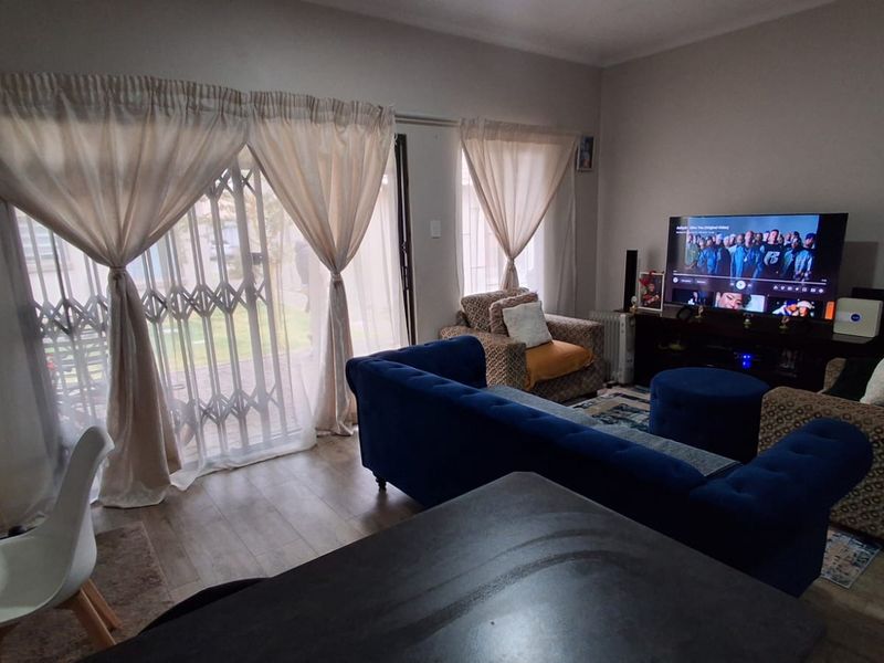 A comfortable living room featuring laminate flooring and a large sliding glass door with a security gate, providing access to the exterior.