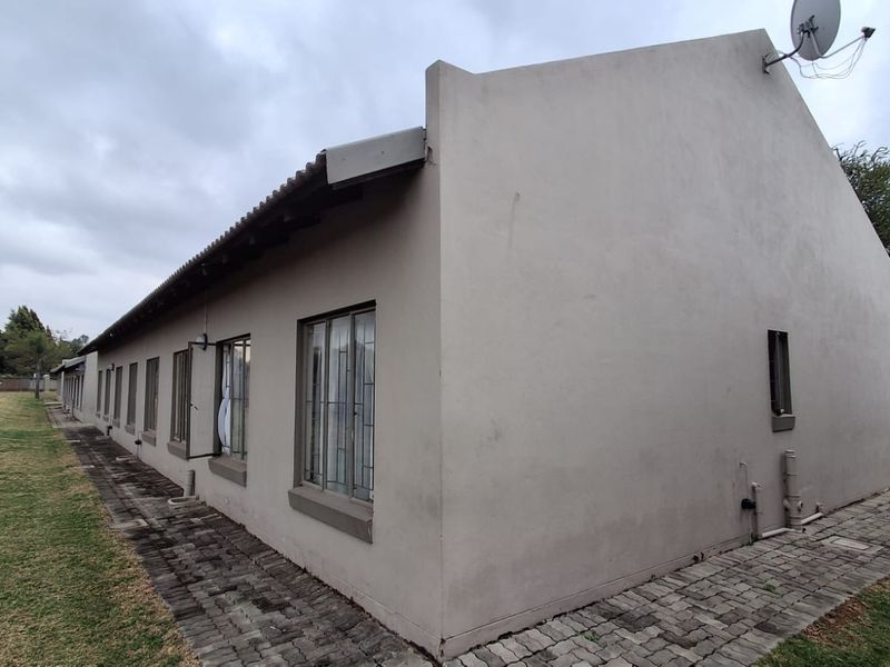 Rear elevation of the townhouse featuring plastered walls, steel frame windows, and a paved walkway along the side of the building.