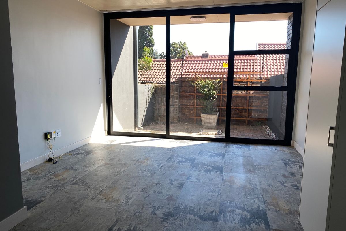A bright, empty living room featuring modern tiled flooring and a large sliding glass door providing access to a private outdoor area.