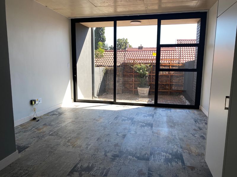 A bright, empty living room featuring modern tiled flooring and a large sliding glass door providing access to a private outdoor area.
