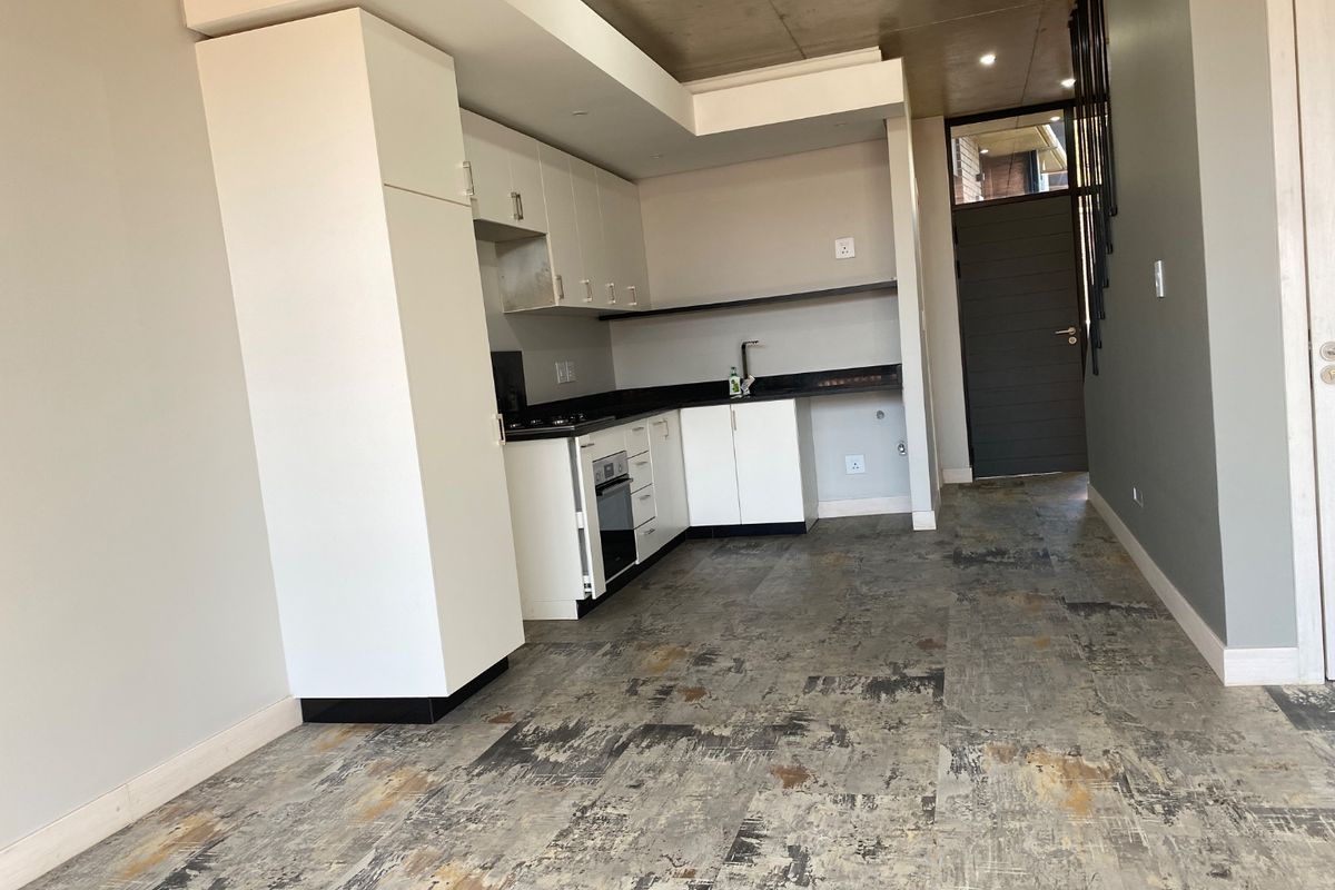 Modern kitchen featuring white cabinetry, dark stone countertops, built-in oven, and hob, set against a contemporary concrete-look tiled floor.