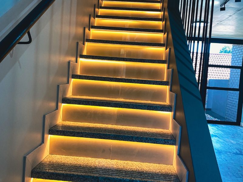 Modern staircase featuring granite treads with integrated LED strip lighting and a sleek metal handrail and balustrade system.