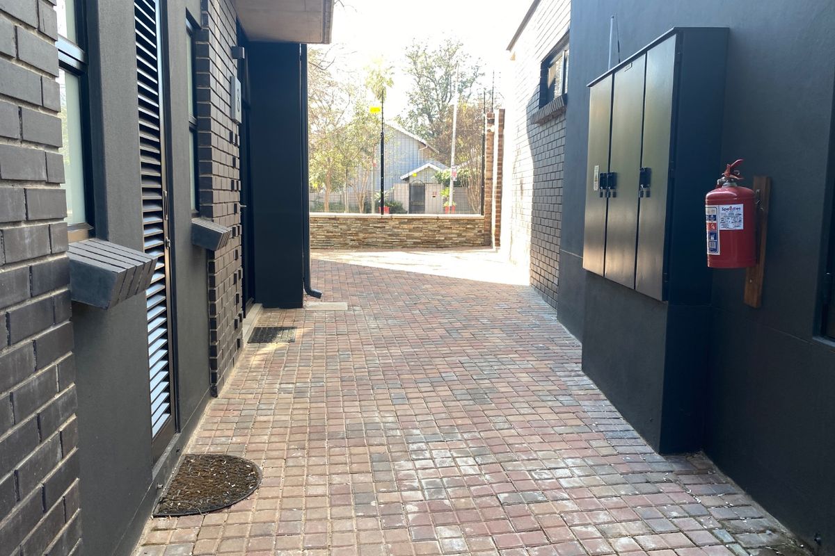 A paved side walkway or rear courtyard area featuring dark brick walls, a utility cabinet, and a mounted fire extinguisher.