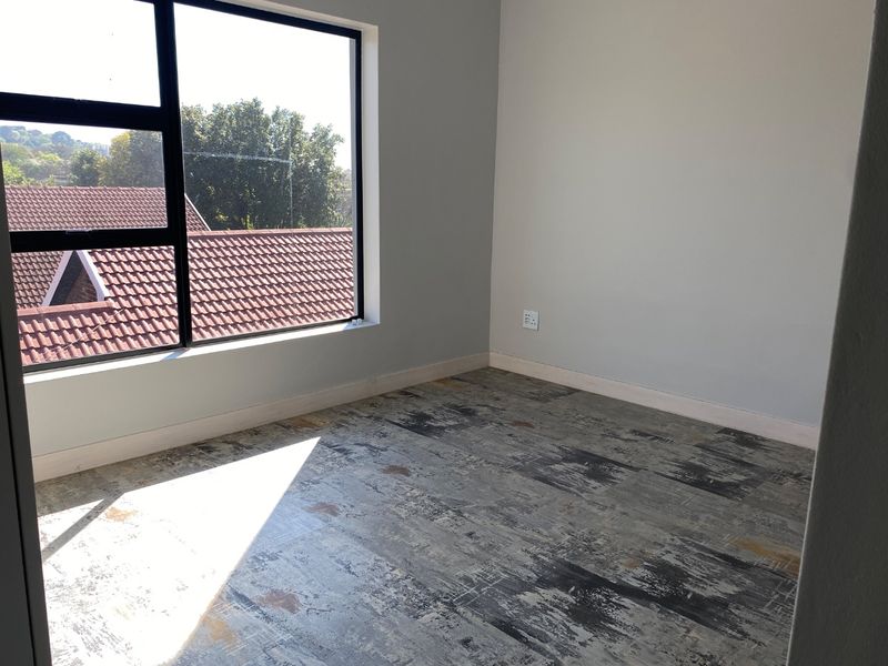An empty bedroom featuring a large window with natural light and unique patterned flooring, ready for personalization.