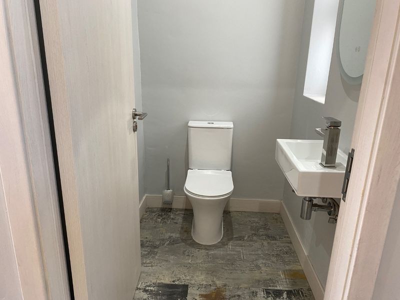 A compact, modern guest bathroom featuring a white toilet, wall-mounted basin with chrome fixtures, and contemporary patterned floor tiling.