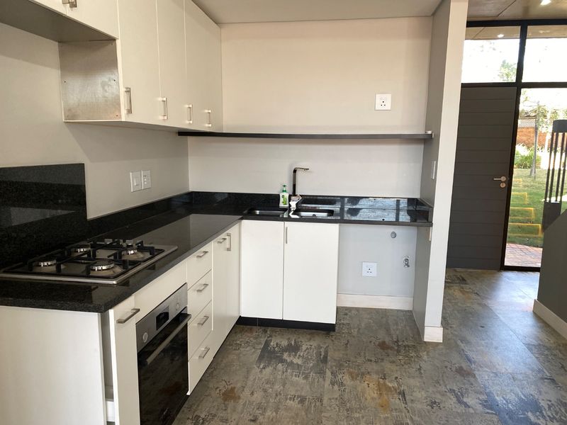 A modern, clean kitchen featuring white cabinetry, dark granite countertops, a gas hob, built-in oven, and durable tiled flooring with direct access to the exterior.