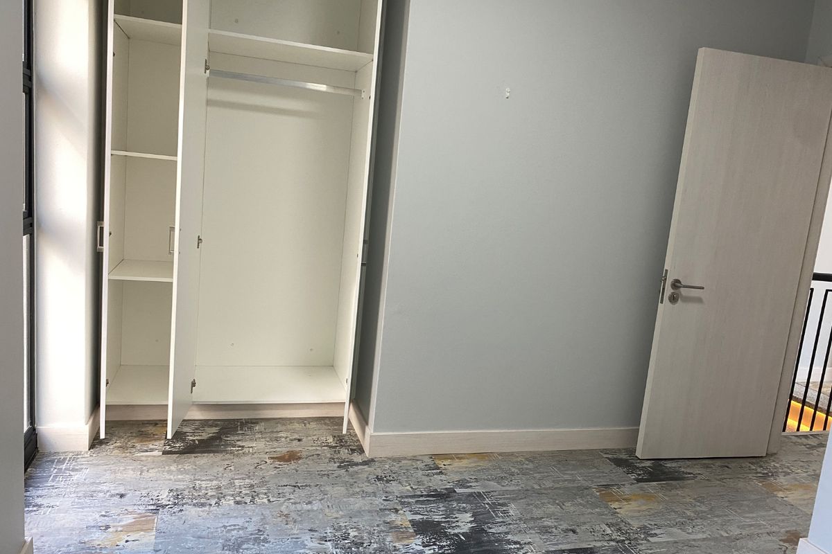 A bright, empty bedroom featuring a built-in wardrobe, modern patterned flooring, and a neutral interior door.