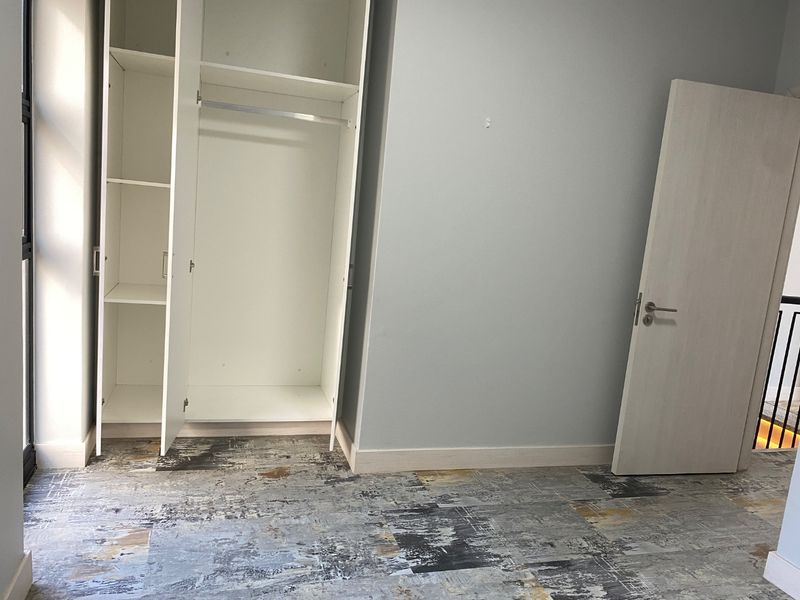 A bright, empty bedroom featuring a built-in wardrobe, modern patterned flooring, and a neutral interior door.