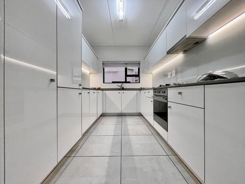 Modern galley-style kitchen featuring high-gloss white cabinetry, integrated appliances, under-cabinet lighting, and sleek tiled flooring.