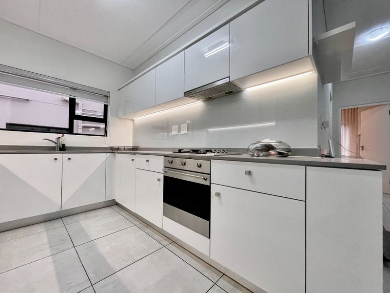 Modern kitchen featuring sleek white cabinetry, stone countertops, integrated stainless steel appliances, and under-cabinet lighting with large format floor tiles.