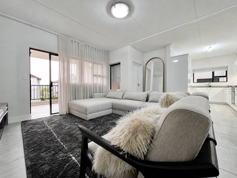 Modern open-plan living area featuring tiled floors, neutral finishes, and a seamless transition to an outdoor balcony through large sliding glass doors.