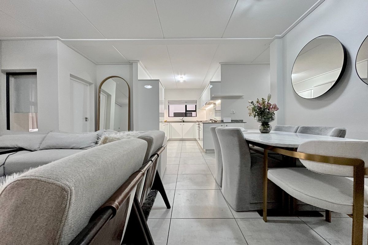 Modern open-plan living and dining area featuring tiled floors, neutral finishes, and a sleek, well-appointed kitchen with integrated cabinetry.