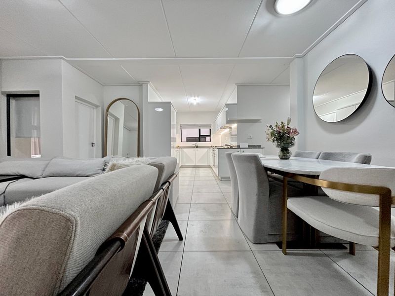 Modern open-plan living and dining area featuring tiled floors, neutral finishes, and a sleek, well-appointed kitchen with integrated cabinetry.