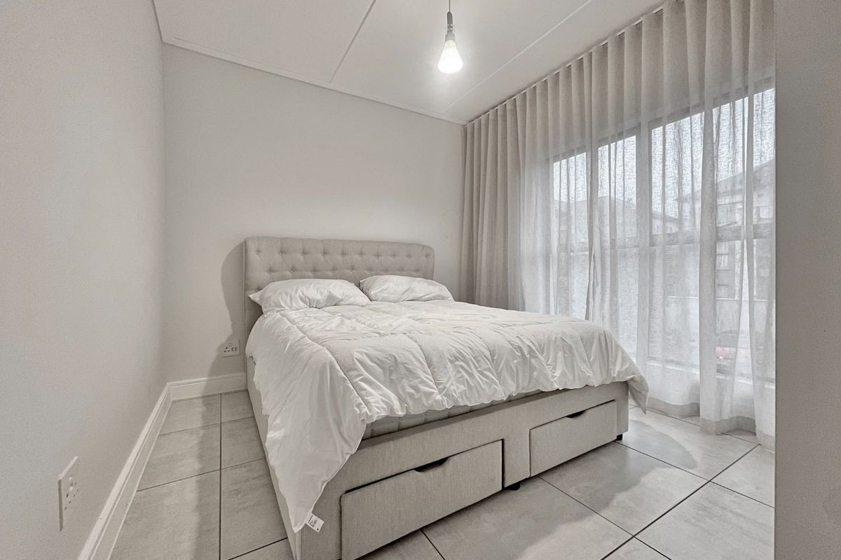 A bright and neutral bedroom featuring tiled flooring, modern pendant lighting, and floor-to-ceiling curtains providing natural light.
