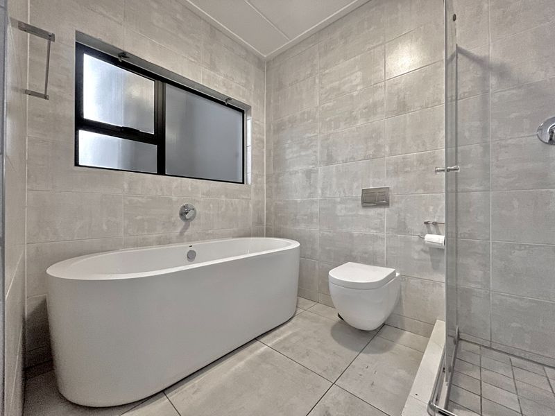 Modern bathroom featuring a sleek freestanding bathtub, wall-mounted toilet, and a glass-enclosed shower with contemporary neutral tiling throughout.