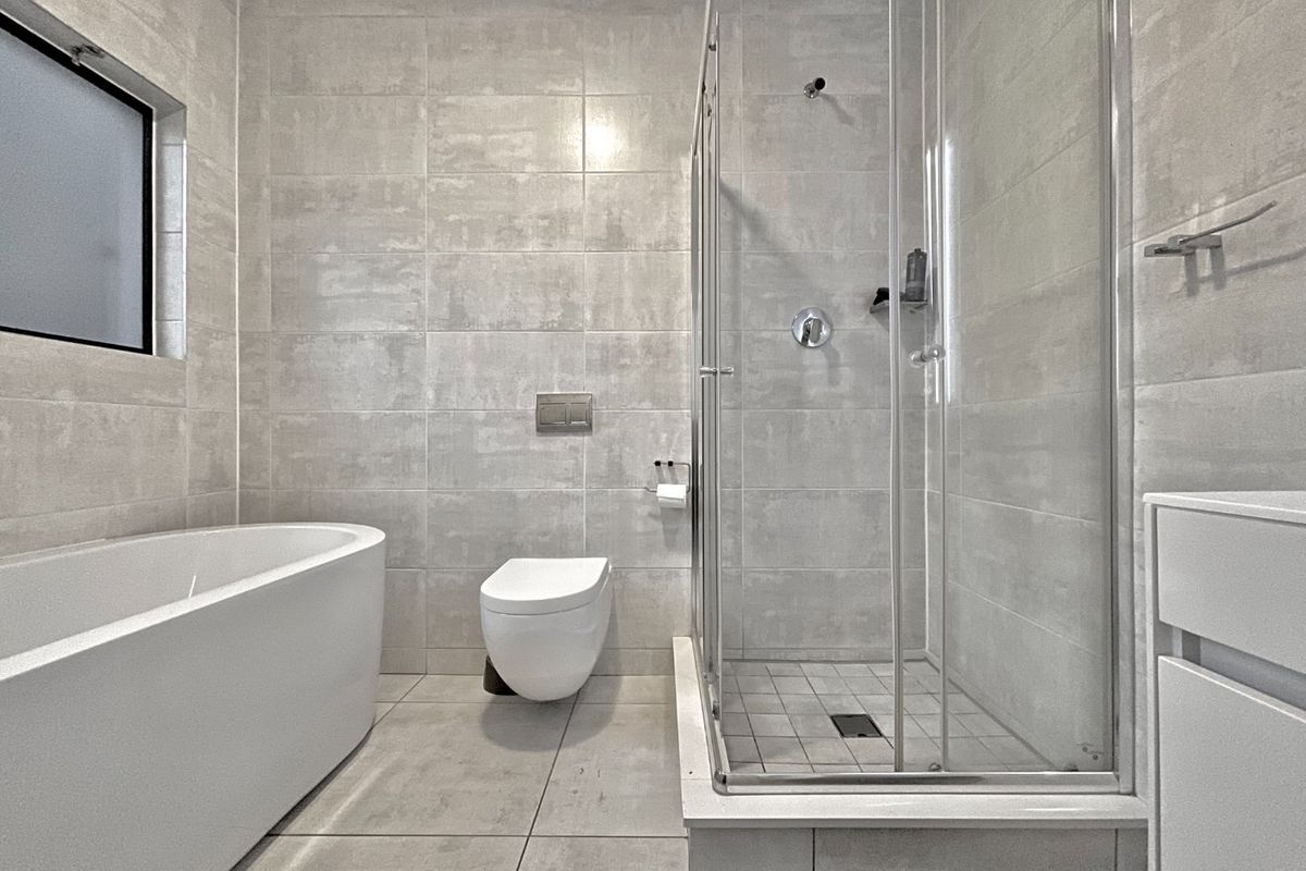 Modern bathroom featuring a sleek freestanding bathtub, a glass-enclosed walk-in shower, and a wall-mounted toilet with neutral floor-to-ceiling tiling.
