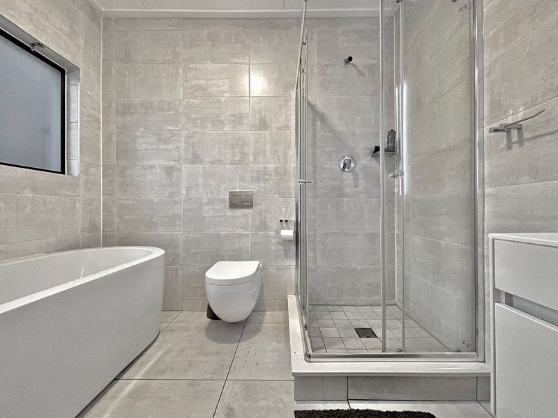 Modern bathroom featuring a sleek freestanding bathtub, a glass-enclosed walk-in shower, and a wall-mounted toilet with neutral floor-to-ceiling tiling.